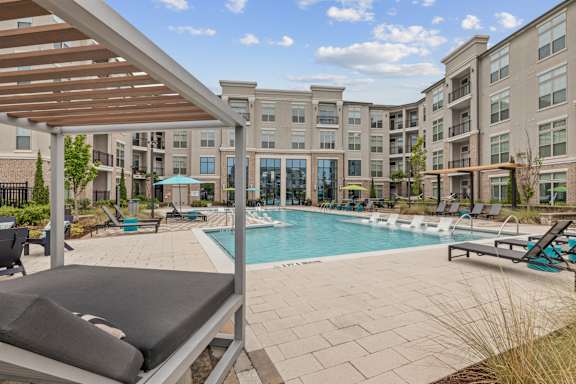 A large outdoor swimming pool with a sun lounger and a building in the background.