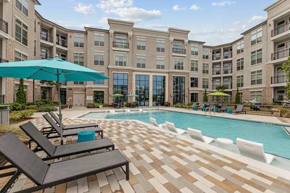 A swimming pool surrounded by lounge chairs and umbrellas in front of a building.