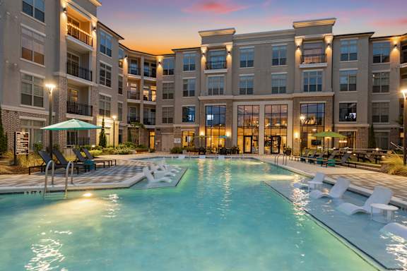 A large swimming pool in front of a building with lounge chairs around it.