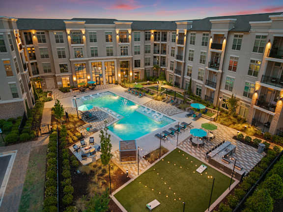 A large apartment complex with a pool and a green lawn.