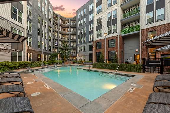 A swimming pool surrounded by lounge chairs in front of apartment buildings.