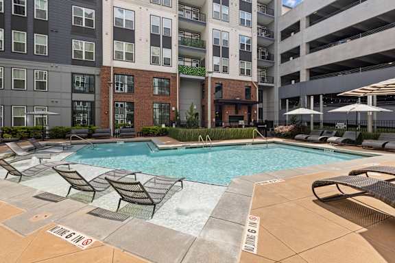 A pool surrounded by lounge chairs and umbrellas in front of a building.