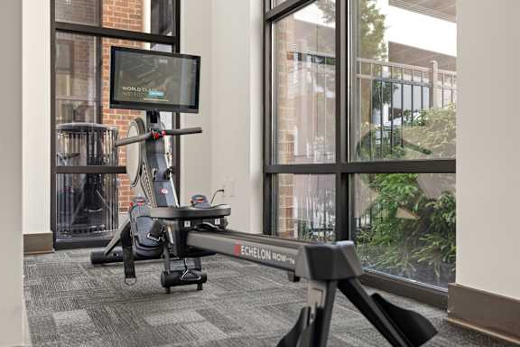 A stationary exercise bike is in a room with a TV and windows.
