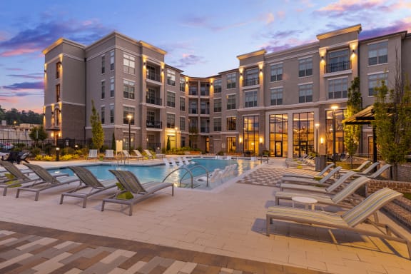 a large swimming pool with chaise lounge chairs and a building in the background
