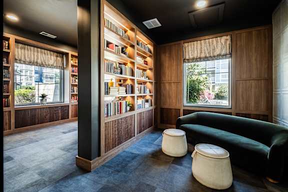 A room with a green couch, a bookshelf, and two poufs.