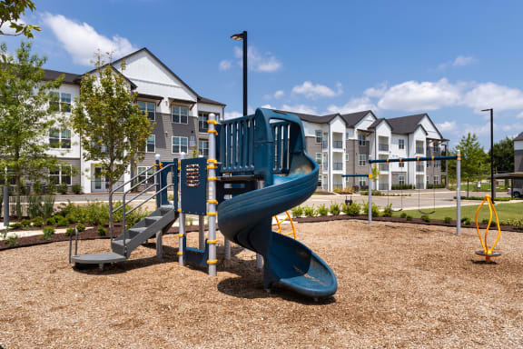 a playground with a blue slide in front of an apartment building