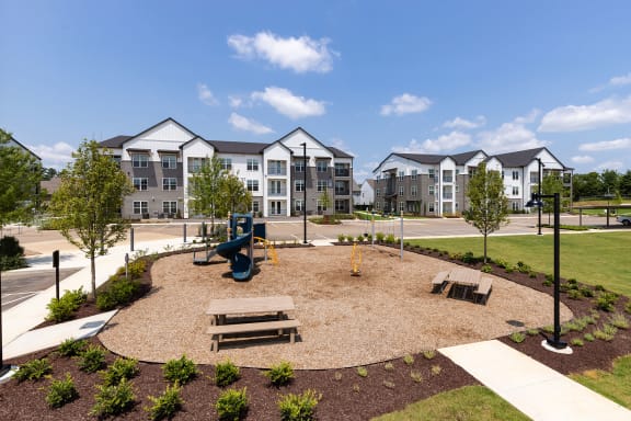 an open park with benches and a playground in front of an apartment building