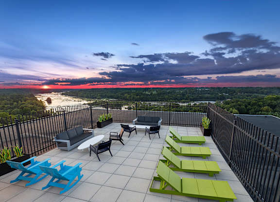 A patio with blue and green chairs overlooks a sunset.