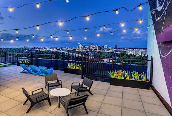 A rooftop patio with a table and chairs overlooking a city skyline at dusk.