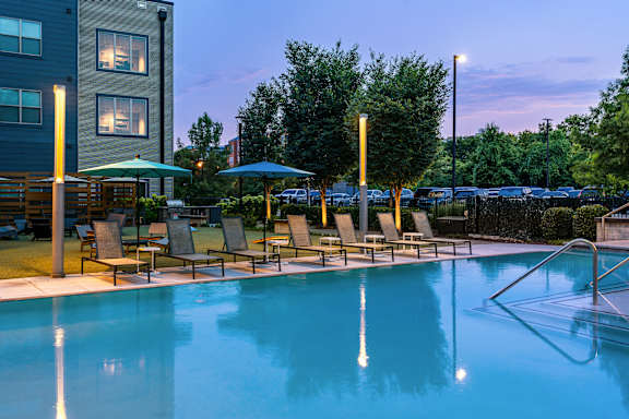 A pool with chairs and umbrellas is lit up at dusk.