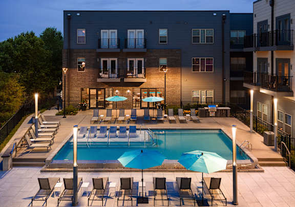 A swimming pool surrounded by chairs and umbrellas in front of a building.