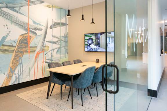 A conference room with a glass wall and a large painting on the wall.