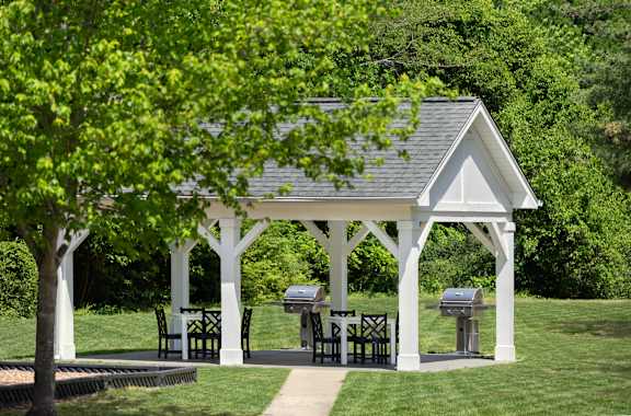 A white gazebo with a table and chairs is surrounded by greenery.