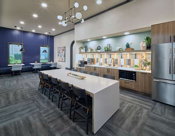 A modern kitchen with a long white island and dark wood flooring.