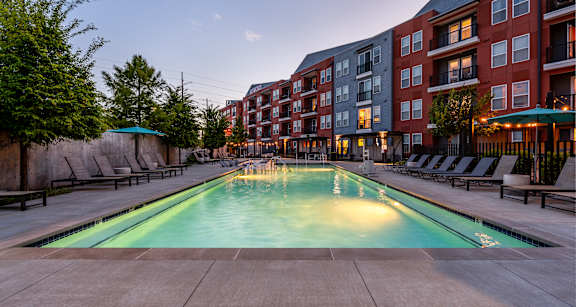 A large outdoor swimming pool surrounded by lounge chairs and trees.