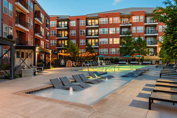 A large swimming pool surrounded by lounge chairs and apartment buildings.