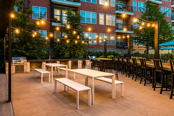 A patio with tables and chairs is lit by string lights.