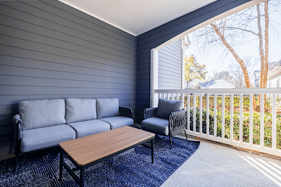 A grey couch and chair are on a patio with a table.
