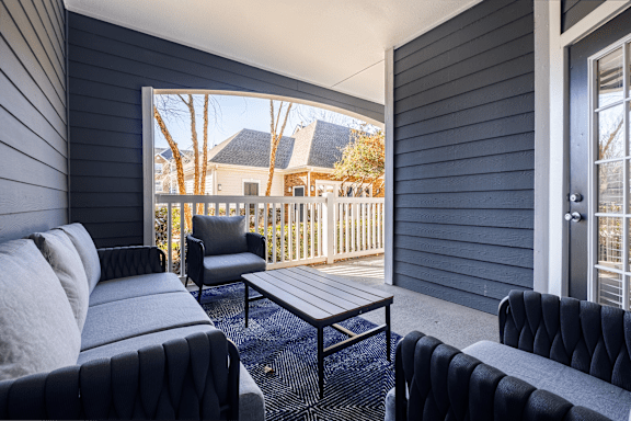 A black couch sits in a living room with a view of a deck and trees outside.