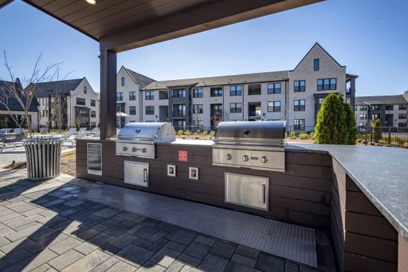 a covered patio with two grills and a building in the background