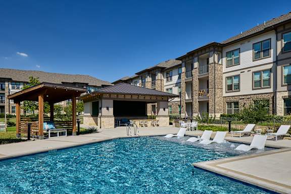 A swimming pool surrounded by lounge chairs and a building in the background.