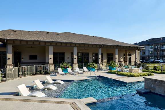 A pool with white chairs and a building in the background.