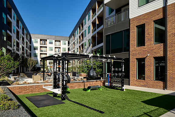 A gym is set up on a grassy area in front of apartment buildings.