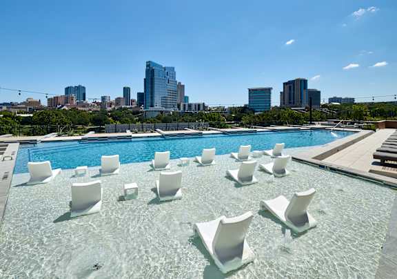 A pool with white chairs and a city skyline in the background.