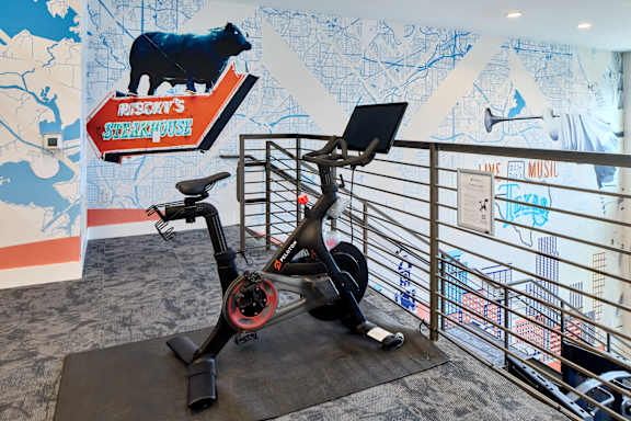 A stationary exercise bike is in front of a wall with a cow on it.