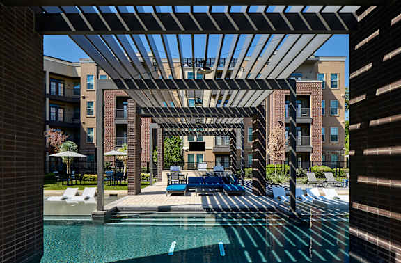 A pool area with a pergola and lounge chairs.