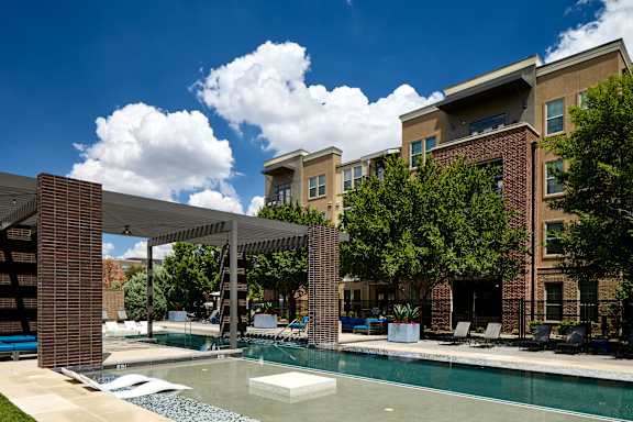 A pool area with a white umbrella and a building in the background.