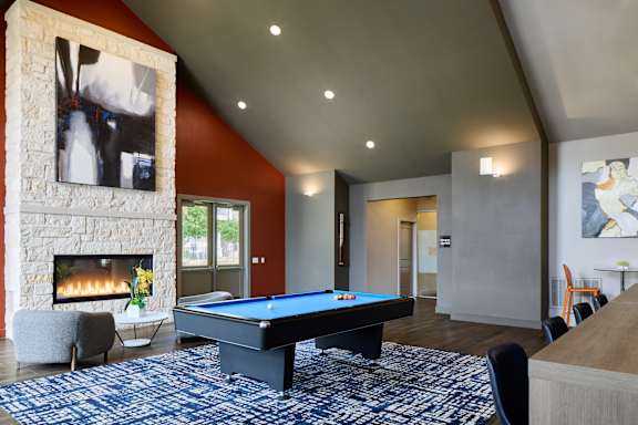 A pool table is in the middle of a room with a fireplace and a chair.