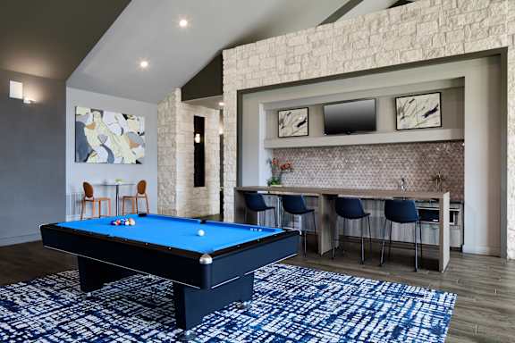 A pool table is in the middle of a room with a stone wall.