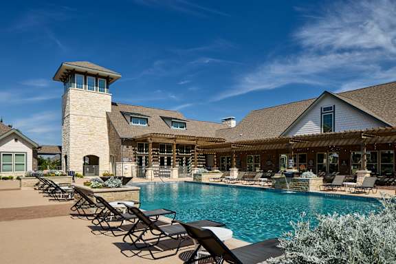 A large house with a pool and lounge chairs.