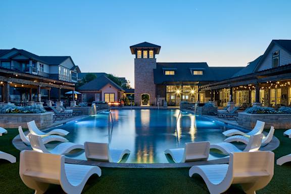A pool surrounded by white chairs in front of a house.