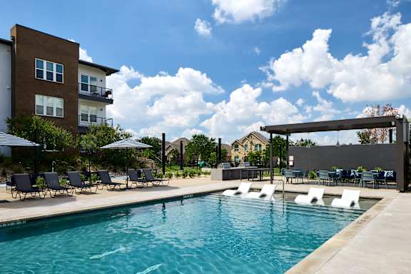 A swimming pool with lounge chairs and umbrellas in front of a building.