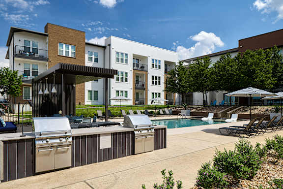 A sunny day at a poolside with a barbecue grill and lounge chairs.