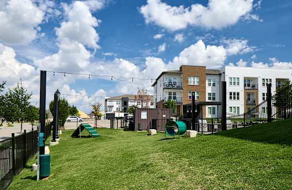 A playground with a slide and swings is surrounded by a fence and apartment buildings.