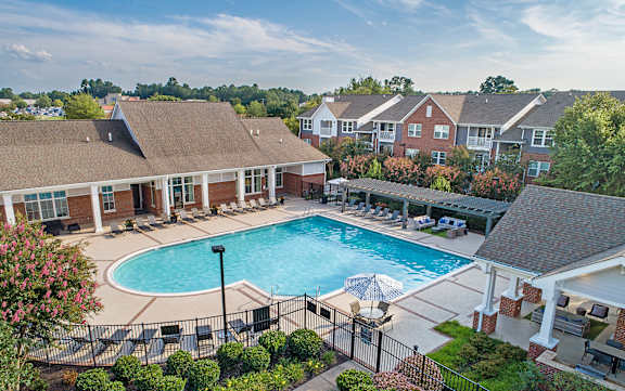A swimming pool surrounded by a black fence and a building with a brown roof.