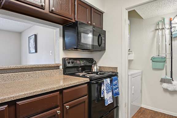 A kitchen with a black stove top oven and a black microwave above it at The Glen Apartments, Lewisville, Texas