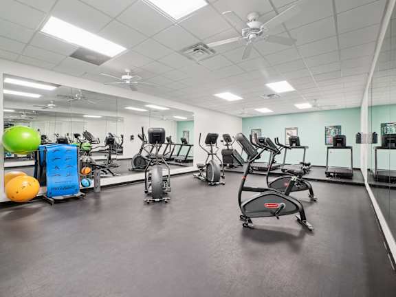 A gym with a variety of exercise equipment including treadmills, stationary bikes, and weights.