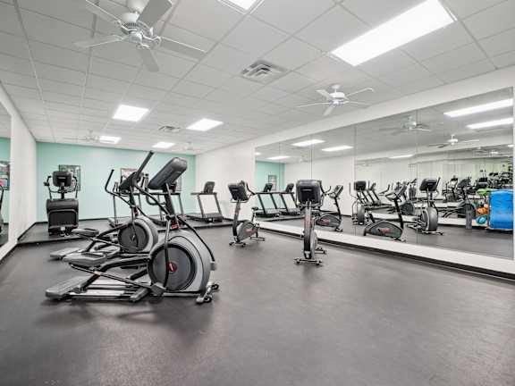 A gym with a variety of exercise equipment including treadmills, stationary bikes, and elliptical machines.