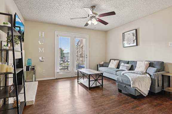 A living room with a grey couch and a ceiling fan at The Glen Apartments, Lewisville, Texas