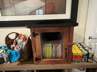 A wooden cabinet with a glass door is open, revealing a collection of DVDs and CDs inside.