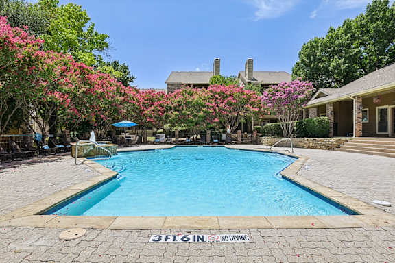A pool surrounded by trees and bushes with a sign that says at The Glen Apartments, Lewisville, Texas