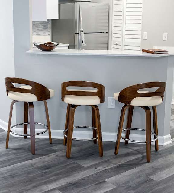 Three wooden bar stools with white cushions are placed in front of a bar.
