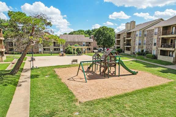 A playground with a green slide and a brown sandbox in the middle of a grassy area at The Glen Apartments, Lewisville, Texas
