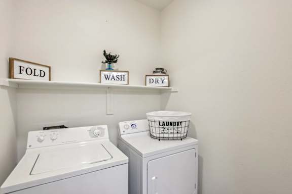 A laundry room with a washer and dryer and a laundry basket on top of the dryer at Sweetwater At Metro North Apartments, Phoenix, Arizona