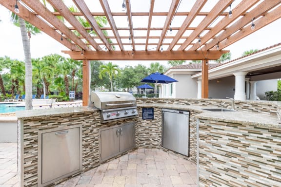 an outdoor kitchen with a pergola and a pool in the background at Heritage Bay, Jensen Beach, FL 34957