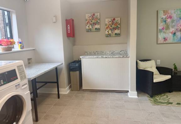 A laundry room with a washer and dryer, a bench, a couch, and a painting on the wall.